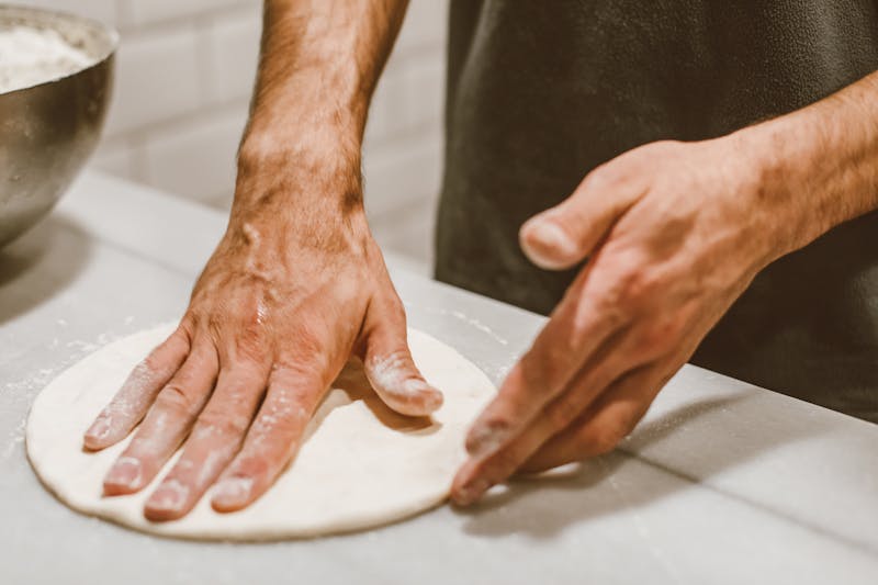 Skilled baker stretching fresh pizza dough by hand